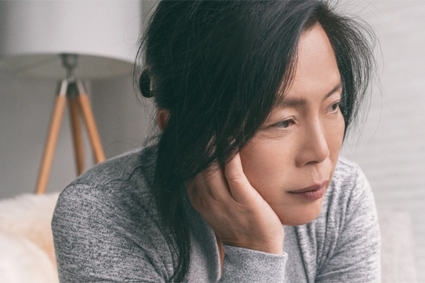 Adrenal-Fatigue-Doctor A middle-aged asian woman sitting on her couch, resting her head on her hand, suffering from adrenal fatigue. Get treatment for adrenal fatigue syndrome from ProCare Wellness Institute in Savannah.