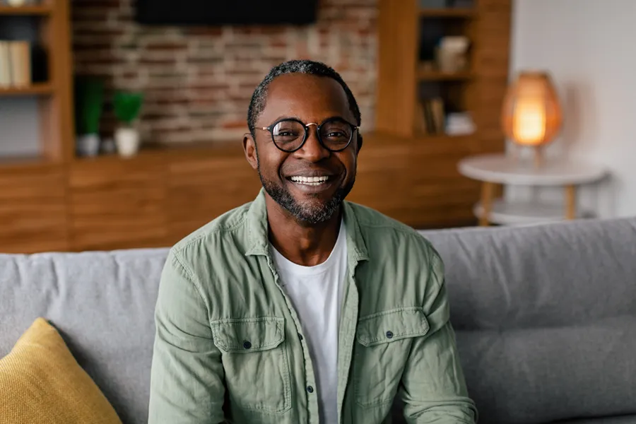 Andropause-Doctor A middle aged black man in a green button up shirt sits on his couch smiling, happy with his treatment for andropause and low testosterone from ProCare Wellness Institute in Savannah.