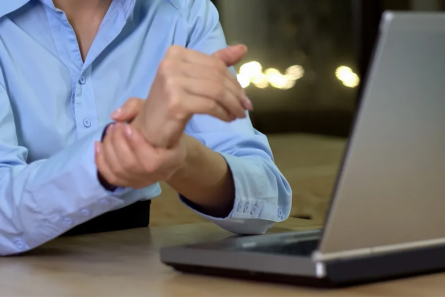 Carpal-Tunnel-Syndrome-Clinic A woman sits in front of her computer rubbing her hand in pain. Schedule treatment for carpal tunnel syndrome from ProCare Wellness Institute in Savannah.