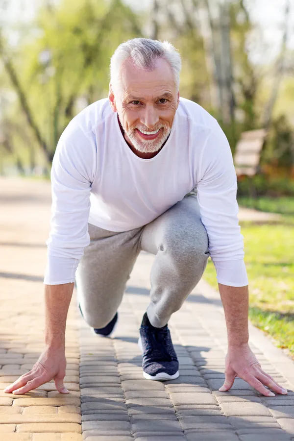 Degenerative-Disc-Disease-Treatment A senior man with grey hair, actively performing a starting block position on a paved path in a park excited to maintain vitality and an active lifestyle because of ProCare Wellness Institute's Degenerative Disc Disease Treatments in Savannah.