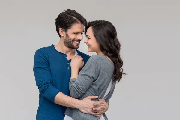 Erectile-Dysfunction-Doctor A man in a blue shirt embracing a woman in a gray shirt smiles due to his successful erectile dysfunction care from ProCare Wellness Institute in Savannah.