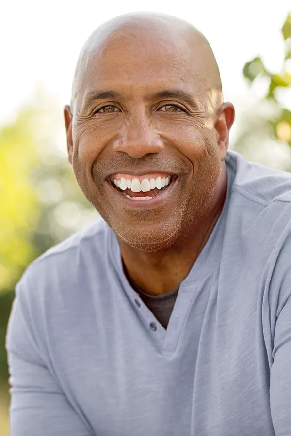 Healthy-Aging-Peptides-Treatment A middle-aged black man in a gray v-neck t-shirt sits outside smiling, happy with the healthy aging peptide treatments from ProCare Wellness Institute in Savannah