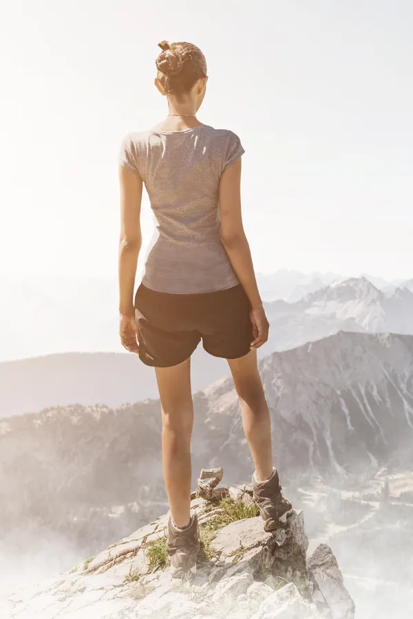 Hyaluronic-Acid-Injections-for-Knee-Pain-Treatment A woman triumphantly standing at the edge of a mountain peak, facing away from the camera and looking out over a vast mountain range after receiving successful Hyaluronic Acid Injections for Knee Pain by ProCare Wellness Institute in Savannah.