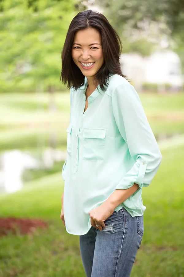 Perimenopause-Treatment A middle-aged brunette woman in a light green button-up shirt stands outside smiling, happy with her perimenopause treatment from ProCare Wellness Institute in Savannah.