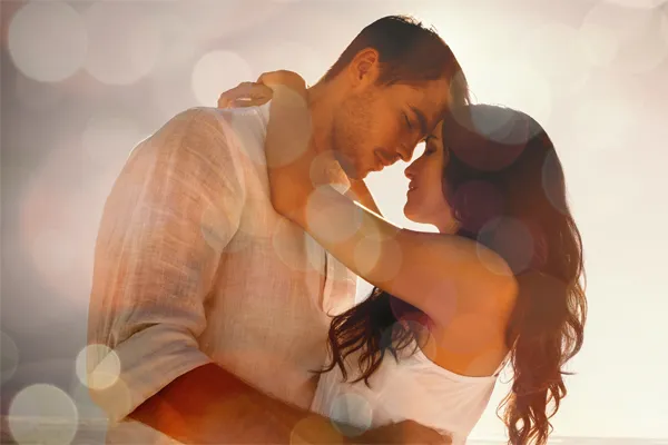 A couple in linen shirts standing in a sparkling light embraces each other with their foreheads touching and eyes closed, happy with their sexual wellness treatments from ProCare Wellness Institute in Savannah.