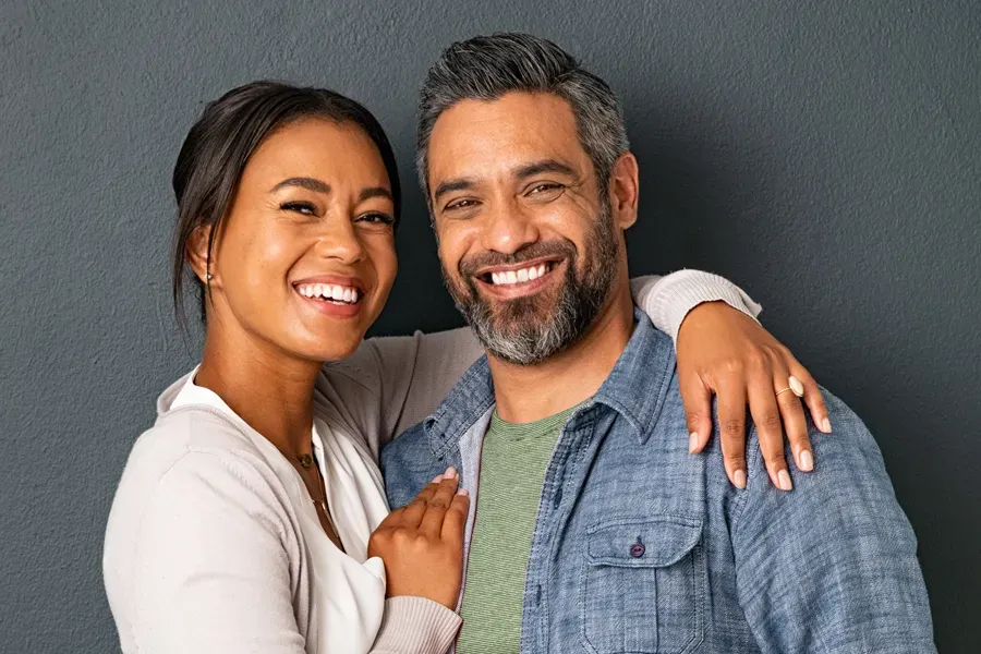 Skin-Rejuvenation-Clinic A middle-aged couple with their arms around each other standing against a gray background and smiling, happy with the skin rejuvenation treatments they received from ProCare Wellness Institute in Savannah.