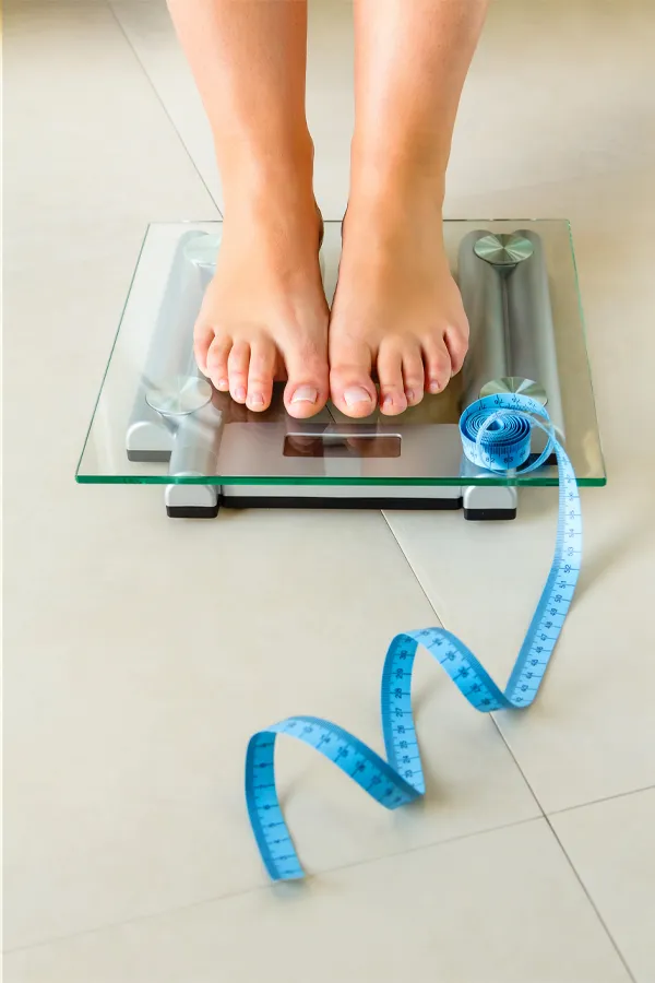 Weight-Loss-Resistance-Treatment Close-up of a woman's feet standing on a scale, with measuring tape by her toes, getting treatment for weight loss resistance from ProCare Wellness Institute in Savannah.
